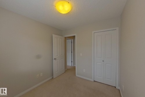 This room features light-colored walls and carpeted flooring, a white bi-fold closet door, and a light-colored interior door - 87 4050 Savaryn Drive, Edmonton, AB - Indoor