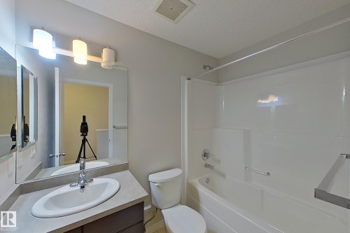 The bathroom features a vanity with an integrated sink and mirror, a toilet, and a combined shower and bathtub - 87 4050 Savaryn Drive, Edmonton, AB - Indoor Photo Showing Bathroom
