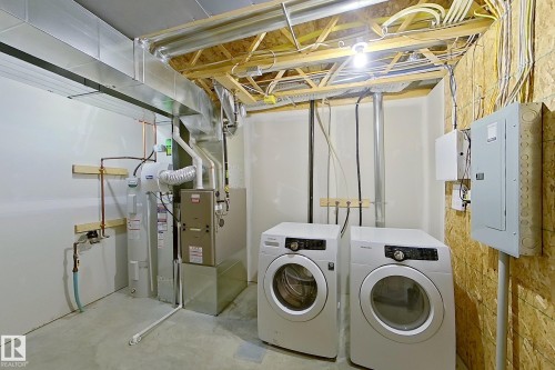 This utility area features a clothes washer and dryer, a water heater, and a furnace, all set on a concrete floor - 87 4050 Savaryn Drive, Edmonton, AB - Indoor Photo Showing Laundry Room