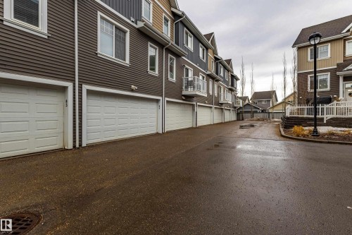 The property features a row of garages with white panel doors, situated along a paved driveway - 87 4050 Savaryn Drive, Edmonton, AB - Outdoor