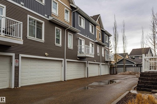 The property features a multi-level exterior with horizontal siding, individual garage doors, and balconies with white railings - 87 4050 Savaryn Drive, Edmonton, AB - Outdoor With Exterior