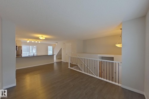 The interior features wood-style flooring, a white railing with dark vertical spindles, and a staircase - 87 4050 Savaryn Drive, Edmonton, AB - Indoor Photo Showing Other Room