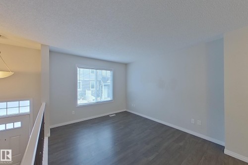 The property features an open living space with neutral paint, dark flooring, and a window with blinds - 87 4050 Savaryn Drive, Edmonton, AB - Indoor Photo Showing Other Room