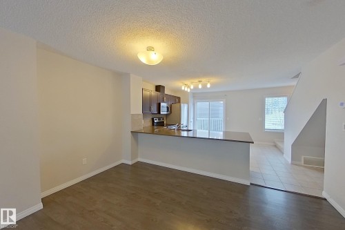 Open concept living area featuring wood laminate flooring, a modern kitchen with dark cabinetry and stainless steel appliances, and a breakfast bar with a stone countertop - 87 4050 Savaryn Drive, Edmonton, AB - Indoor