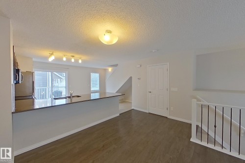 Spacious open-concept interior featuring wood-look flooring, a kitchen island with a sink and ample counter space, and a sliding glass door providing external access - 87 4050 Savaryn Drive, Edmonton, AB - Indoor Photo Showing Other Room