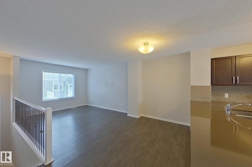 Open concept living area featuring dark wood-style flooring, a large window with blinds, and a kitchen counter with an undermount sink and a gooseneck faucet - 87 4050 Savaryn Drive, Edmonton, AB - Indoor Photo Showing Other Room