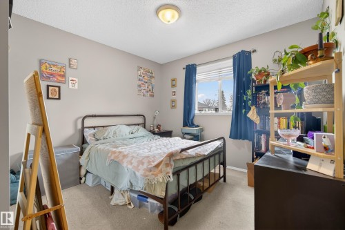 This bedroom features light gray walls, a window with blue curtains, and a ceiling light fixture - 8109 85 Street, Edmonton, AB - Indoor Photo Showing Bedroom