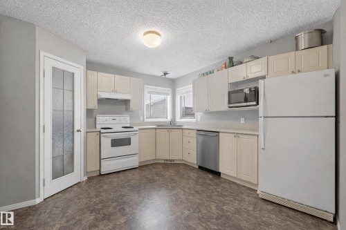 The kitchen features light-toned cabinetry, a white refrigerator, a white range, a stainless steel dishwasher, and a window with a view - 8109 85 Street, Edmonton, AB - Indoor Photo Showing Kitchen