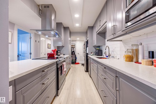 The kitchen features extensive gray cabinetry, light-colored countertops, a stainless steel range hood, and a built-in microwave - 803 12303 Jasper Avenue, Edmonton, AB - Indoor Photo Showing Kitchen