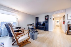 The living area features light-toned flooring, a large window providing natural light, and a spacious layout - 