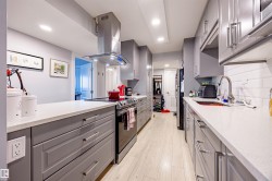 The kitchen features gray cabinetry, white countertops, a stainless steel range hood, and a white subway tile backsplash - 