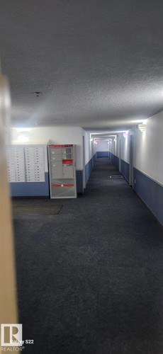 A well-lit interior hallway featuring wall-mounted lighting fixtures, a textured ceiling, and a dark carpeted floor - 204 11218 80 Street, Edmonton, AB - Indoor Photo Showing Other Room