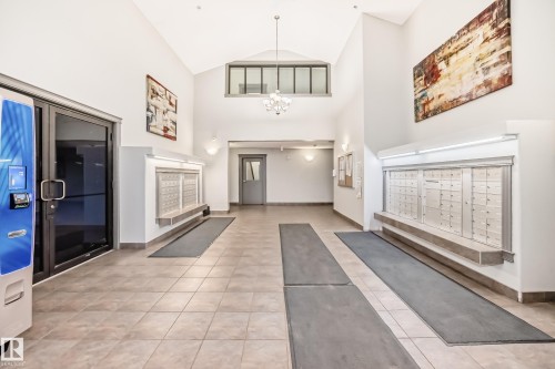 The property features a spacious lobby with tile flooring, a high vaulted ceiling, and two large banks of mailboxes - 102 111 Edwards Drive, Edmonton, AB - Indoor Photo Showing Other Room With Fireplace