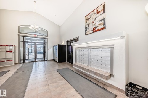 The property features a spacious lobby with tile flooring, high vaulted ceilings, and a contemporary chandelier - 102 111 Edwards Drive, Edmonton, AB - Indoor Photo Showing Other Room