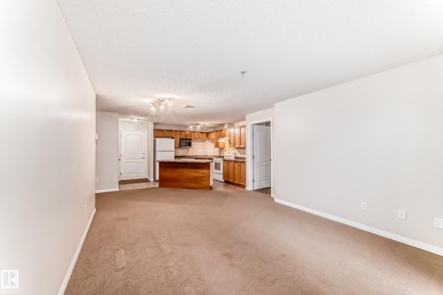 Open concept living area featuring light-colored walls and carpeted flooring - 102 111 Edwards Drive, Edmonton, AB - Indoor Photo Showing Other Room