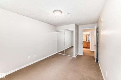 This room features neutral-toned carpeting, light-colored walls, and a ceiling light fixture - 102 111 Edwards Drive, Edmonton, AB - Indoor Photo Showing Other Room