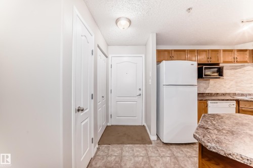 The property features a kitchen with wood cabinetry, a microwave, and a refrigerator - 102 111 Edwards Drive, Edmonton, AB - Indoor Photo Showing Kitchen