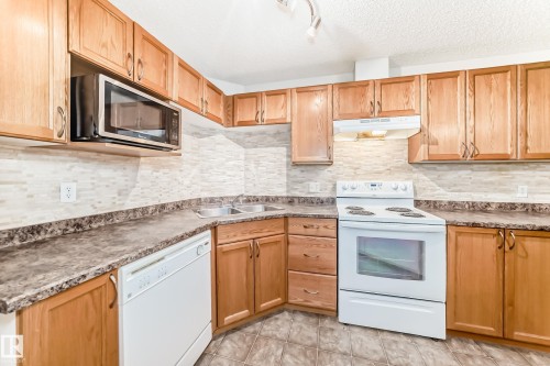 The kitchen features wooden cabinetry, patterned countertops, and a mosaic tile backsplash - 102 111 Edwards Drive, Edmonton, AB - Indoor Photo Showing Kitchen With Double Sink