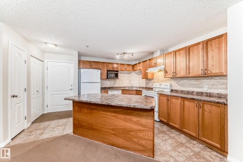 The kitchen features wood cabinetry, a central island with a countertop, and tiled flooring - 102 111 Edwards Drive, Edmonton, AB - Indoor Photo Showing Kitchen
