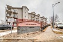 The property features a multi-story building with balconies, a decorative stone and stucco sign, and a paved sidewalk - 102 111 Edwards Drive, Edmonton, AB  - Outdoor 
