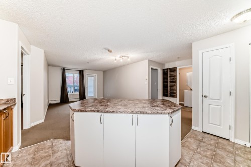 The kitchen features a functional island with a laminate countertop and white cabinetry, complemented by tile flooring - 102 111 Edwards Drive, Edmonton, AB - Indoor Photo Showing Kitchen