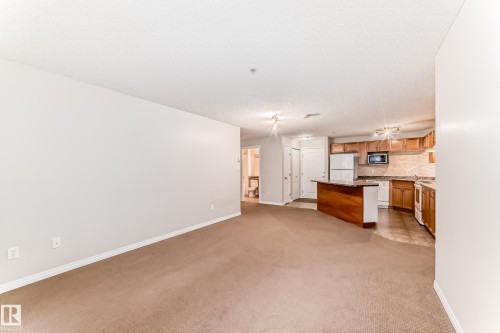 Open concept living space featuring neutral colored walls, carpeting, and a kitchen with wooden cabinetry and a breakfast bar - 102 111 Edwards Drive, Edmonton, AB - Indoor