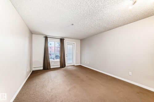 Living area featuring light-colored walls, brown carpet, and a window with curtains - 102 111 Edwards Drive, Edmonton, AB - Indoor Photo Showing Other Room