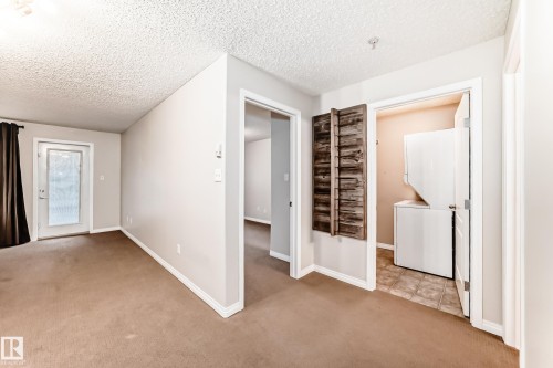 The property features an in-unit laundry area with a stacked washer and dryer, along with a door leading to the exterior - 102 111 Edwards Drive, Edmonton, AB - Indoor Photo Showing Other Room