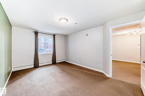 This room features a window with dark curtains, a textured ceiling with a flush-mount light fixture, and carpeted floors - 102 111 Edwards Drive, Edmonton, AB - Indoor Photo Showing Other Room