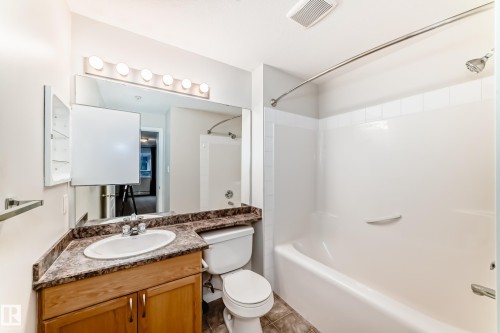 The bathroom features a vanity with a countertop and an integrated sink, a toilet, and a combination shower and bathtub - 102 111 Edwards Drive, Edmonton, AB - Indoor Photo Showing Bathroom