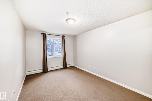 This room features light-colored walls, brown carpeting, and a window with brown curtains - 102 111 Edwards Drive, Edmonton, AB - Indoor Photo Showing Other Room