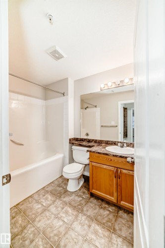 Bathroom featuring a bathtub with shower, a toilet, a vanity with a white sink, and tiled flooring - 102 111 Edwards Drive, Edmonton, AB - Indoor Photo Showing Bathroom