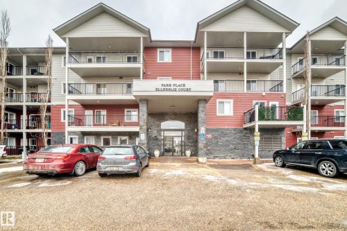 The property features a multi-story exterior with red and grey siding, stone detailing, and balconies with black railings - 102 111 Edwards Drive, Edmonton, AB - Outdoor With Facade