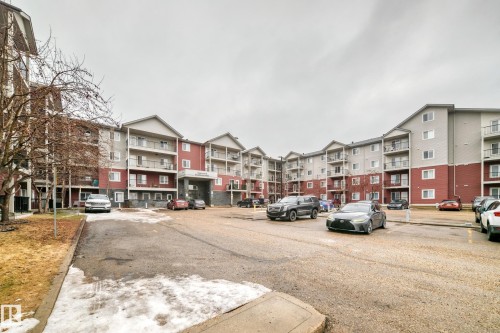 The property features a multi-story building with a red and grey exterior, complemented by white window frames and individual balconies - 102 111 Edwards Drive, Edmonton, AB - Outdoor With Facade