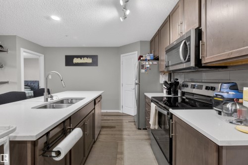Well-appointed kitchen featuring a large island with a double basin sink, ample counter space, and stainless steel appliances - 134 148 Ebbers Boulevard, Edmonton, AB - Indoor Photo Showing Kitchen With Double Sink With Upgraded Kitchen