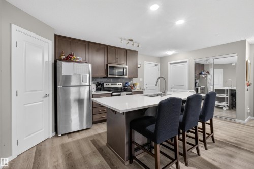 The kitchen features sleek wood cabinetry, stainless steel appliances, and a central island with a white countertop and seating - 134 148 Ebbers Boulevard, Edmonton, AB - Indoor Photo Showing Kitchen With Upgraded Kitchen