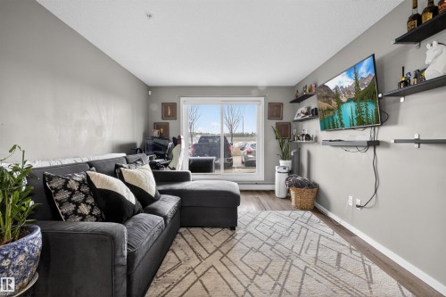 Living area featuring light grey walls, dark wood-style flooring, and a sliding glass door providing natural light - 134 148 Ebbers Boulevard, Edmonton, AB - Indoor Photo Showing Living Room