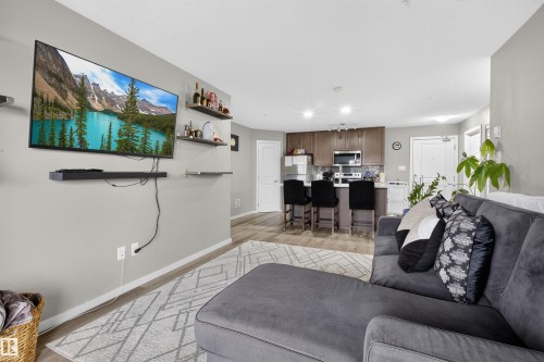 The open concept living area features light-colored walls and flooring, with a kitchen visible in the background - 134 148 Ebbers Boulevard, Edmonton, AB - Indoor Photo Showing Living Room