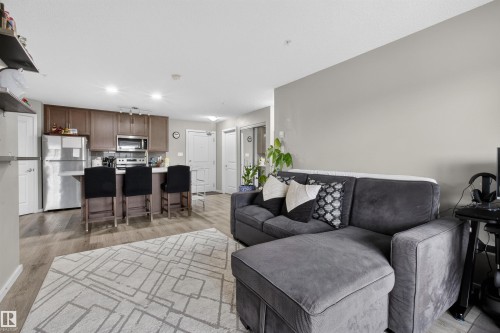 Open concept living area featuring wood-style flooring and a kitchen with stainless steel appliances, a breakfast bar, and wood cabinetry - 134 148 Ebbers Boulevard, Edmonton, AB - Indoor Photo Showing Living Room