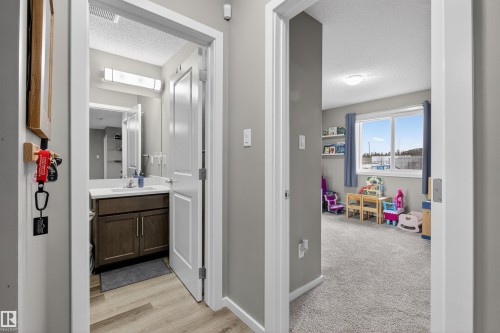 The property features a bathroom with a vanity, mirror, and overhead lighting, alongside a room with carpeted flooring and large windows - 134 148 Ebbers Boulevard, Edmonton, AB - Indoor