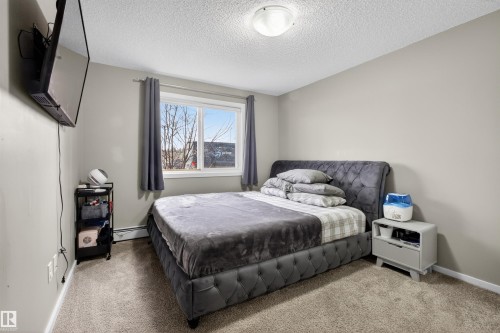This room features neutral-toned walls, carpeted flooring, and a large window providing natural light - 134 148 Ebbers Boulevard, Edmonton, AB - Indoor Photo Showing Bedroom