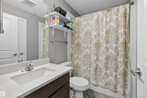 Bathroom featuring a vanity with a white countertop and an integrated sink, a large wall mirror, and white wall shelving - 134 148 Ebbers Boulevard, Edmonton, AB - Indoor Photo Showing Bathroom