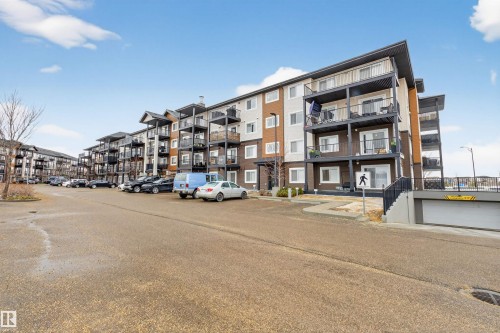 The property features a multi-story building with balconies, an exterior with brown and beige siding, and a paved parking area - 134 148 Ebbers Boulevard, Edmonton, AB - Outdoor With Facade