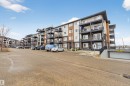 The property features a multi-story building with balconies, an exterior with brown and beige siding, and a paved parking area - 134 148 Ebbers Boulevard, Edmonton, AB  - Outdoor With Facade 