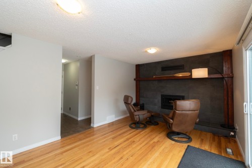 This inviting living area features warm hardwood floors, a striking fireplace with a dark stone surround, and a wooden mantel - 54 Beaverbrook Crescent, St. Albert, AB - Indoor With Fireplace