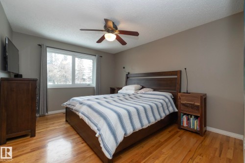 This sleeping area features hardwood flooring, a ceiling fan with integrated lighting, and a large window with drapes - 54 Beaverbrook Crescent, St. Albert, AB - Indoor Photo Showing Bedroom