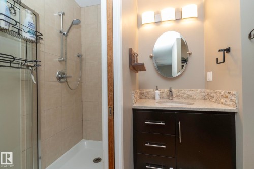 Bathroom featuring a shower with tiled walls and a handheld showerhead, a dark wood vanity with a light-colored countertop and backsplash, an oval mirror, and a three-light fixture - 54 Beaverbrook Crescent, St. Albert, AB - Indoor Photo Showing Bathroom