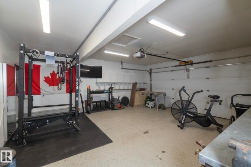 The property features a garage with a roll-up garage door, overhead lighting, and a speckled floor finish - 54 Beaverbrook Crescent, St. Albert, AB - Indoor Photo Showing Garage
