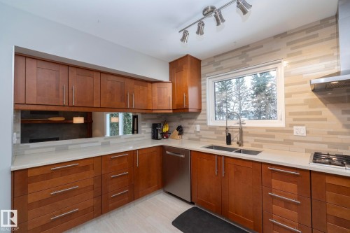 The kitchen features wood cabinetry, light countertops, and a window with an exterior view of trees - 54 Beaverbrook Crescent, St. Albert, AB - Indoor Photo Showing Kitchen With Double Sink