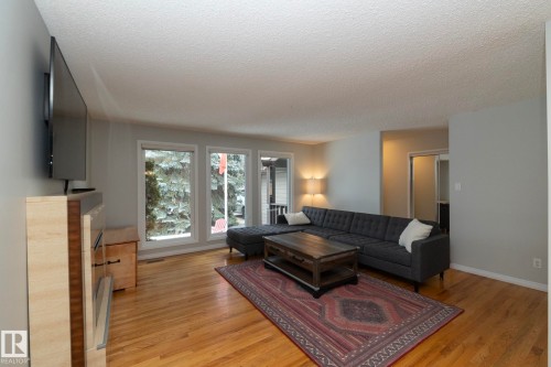 This inviting living area features hardwood floors and large windows that offer natural light and views of the surrounding trees - 54 Beaverbrook Crescent, St. Albert, AB - Indoor Photo Showing Living Room